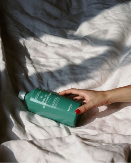 Hand holding a green bottle on a textured surface