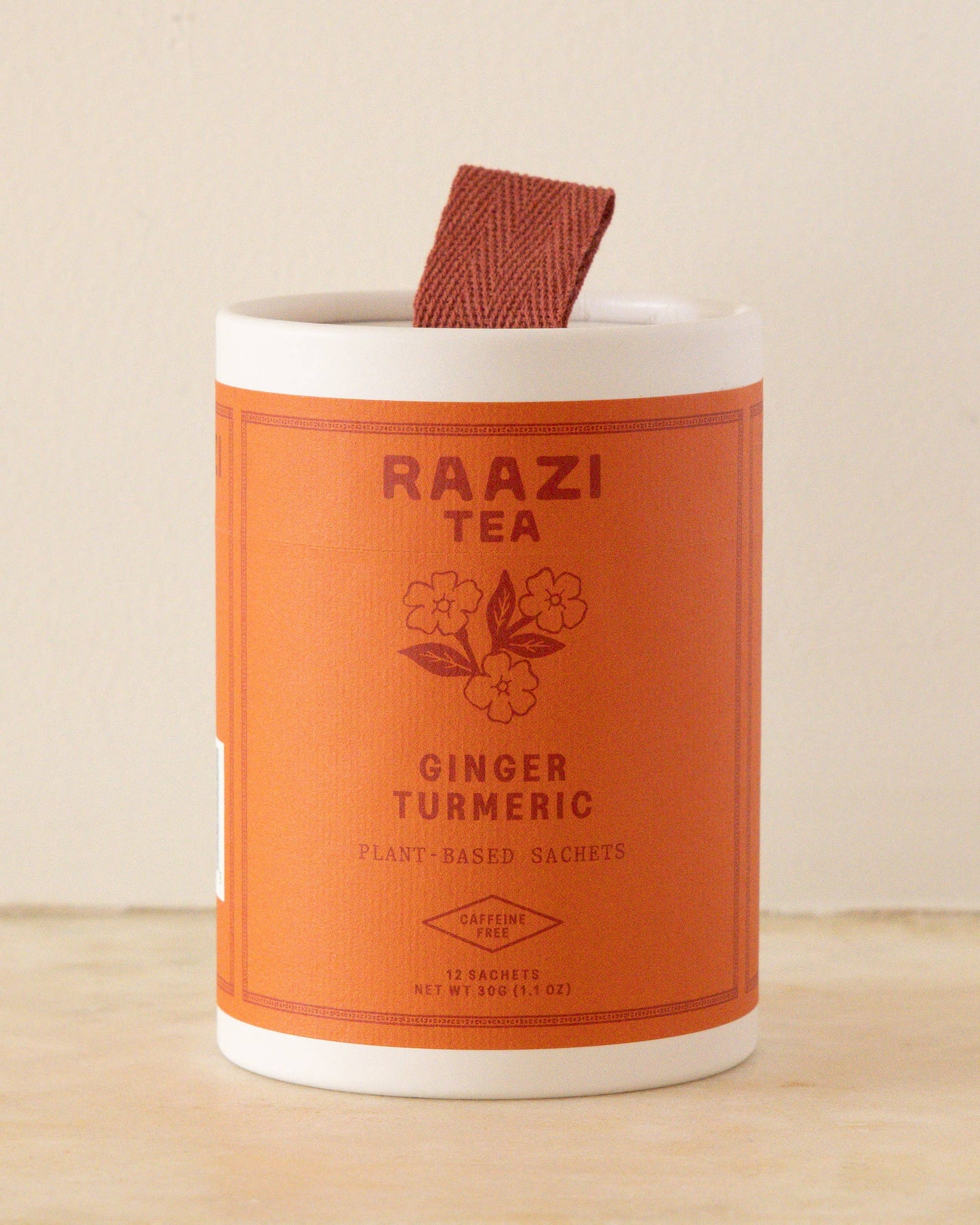 Orange and white container of Raazi Tea Ginger Turmeric on a beige background