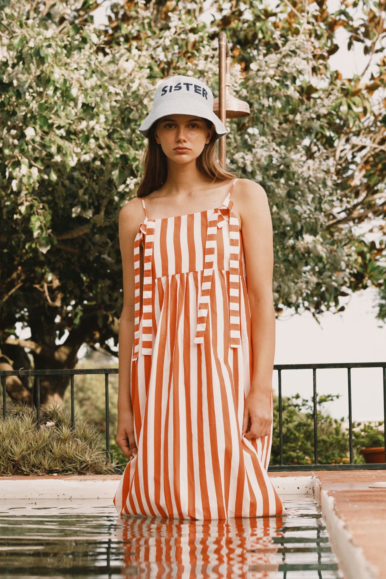 Woman wearing a striped dress and bucket hat with 'SISTER' text outdoors.