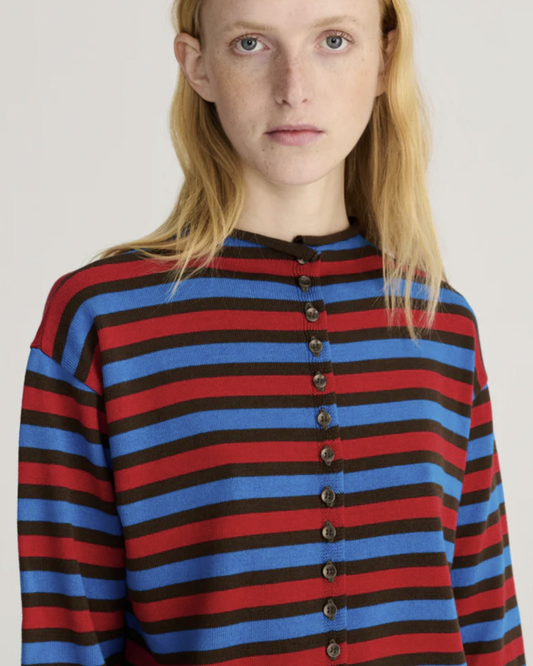 A close-up of a model wearing a long-sleeve knit top with horizontal stripes in red, blue, and black, featuring a button-up front.