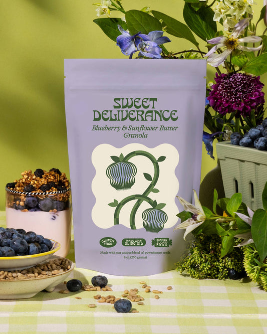 Sweet Deliverance Blueberry & Sunflower Butter Granola package with granola and blueberries on a green checkered tablecloth.